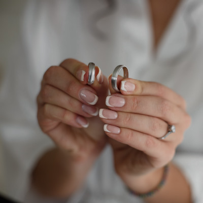 Foto a colori delle mani di una sposa che tengono strette tra le dita due fedi nuziali